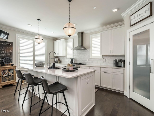 1610 Draper View Loop Unit 101, Raleigh, NC 27608 - kitchen featuring wall chimney range hood, an island with sink, decorative backsplash, white cabinets, and ornamental molding
