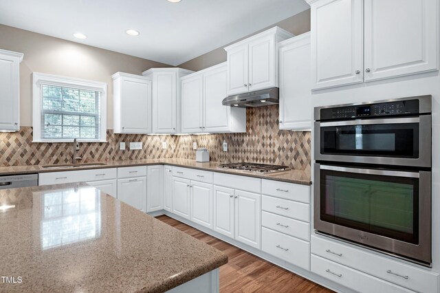 112 Briarfield Dr, Apex, NC 27502 - kitchen featuring appliances with stainless steel finishes, under cabinet range hood, light wood-style flooring, white cabinetry, and light stone countertops