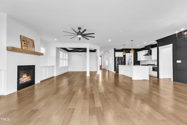 121 Nate Ct, Wake Forest, NC 27587 - unfurnished living room with a brick fireplace, a decorative wall, ceiling fan, light wood-type flooring, and a sink