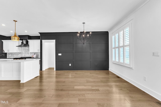 121 Nate Ct, Wake Forest, NC 27587 - kitchen featuring wall chimney exhaust hood, a decorative wall, a chandelier, white cabinetry, and tasteful backsplash