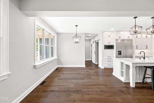390 Lake Magnolia Way, Smithfield, NC 27577 - kitchen with a barn door, built in appliances, baseboards, a chandelier, and white cabinets