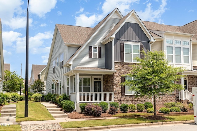 921 Rosepine Dr, Cary, NC 27519 - view of front facade featuring board and batten siding, stone siding, covered porch, a shingled roof, and a front lawn