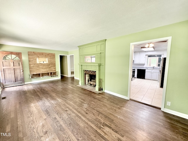 322 S Dixon Ave, Cary, NC 27511 - unfurnished living room with wood finished floors, a tiled fireplace, baseboards, a sink, and a textured ceiling