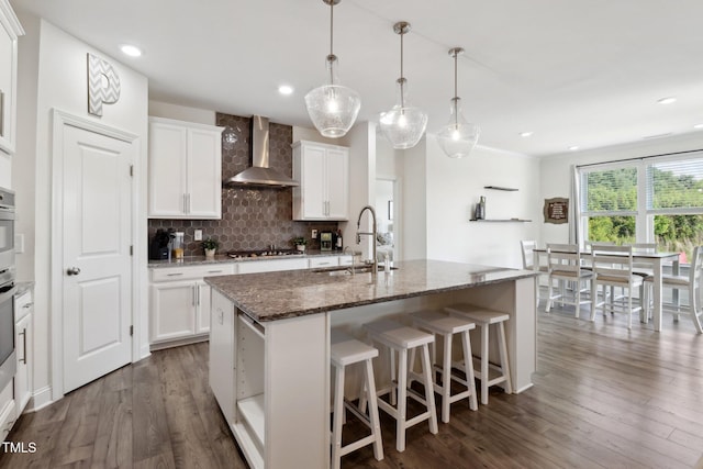 404 Porterfield Dr, Youngsville, NC 27596 - kitchen with wall chimney exhaust hood, an island with sink, decorative backsplash, stainless steel gas cooktop, and dark wood finished floors