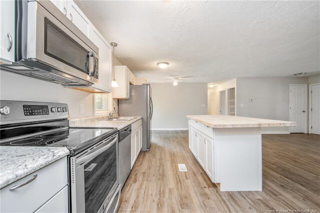 6313 Belle Terre Ct, Fayetteville, NC 28304 - kitchen featuring appliances with stainless steel finishes, a kitchen island, light wood-style floors, a textured ceiling, and white cabinets