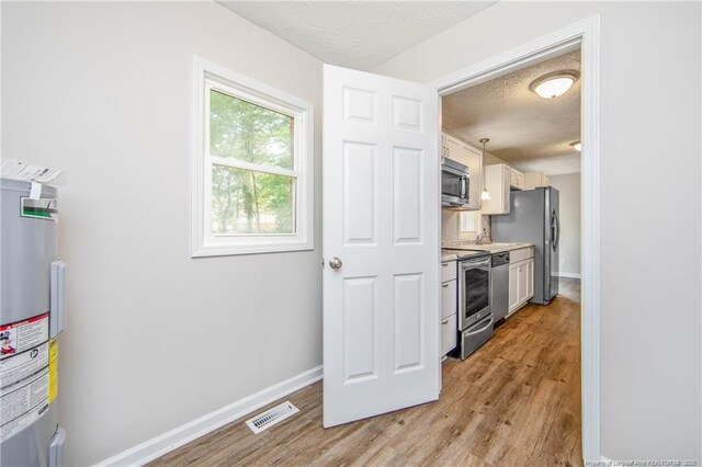 6313 Belle Terre Ct, Fayetteville, NC 28304 - kitchen with stainless steel appliances, a textured ceiling, electric water heater, light wood finished floors, and baseboards