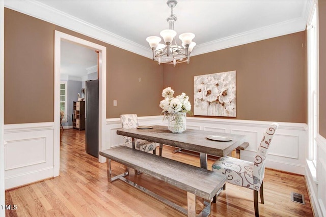 1128 Neuse Ridge Dr, Clayton, NC 27527 - dining room featuring a chandelier, a wainscoted wall, crown molding, light wood finished floors, and a decorative wall