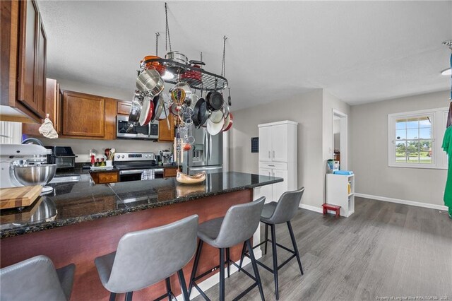 701 Dandridge Dr, Fayetteville, NC 28304 - kitchen with appliances with stainless steel finishes, a peninsula, wood finished floors, brown cabinetry, and a breakfast bar