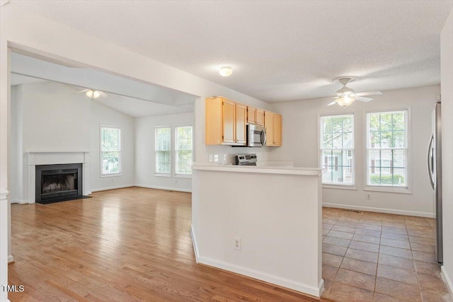 205 Mint Hill Dr, Cary, NC 27519 - kitchen featuring a ceiling fan, light brown cabinetry, stainless steel appliances, a fireplace with flush hearth, and vaulted ceiling