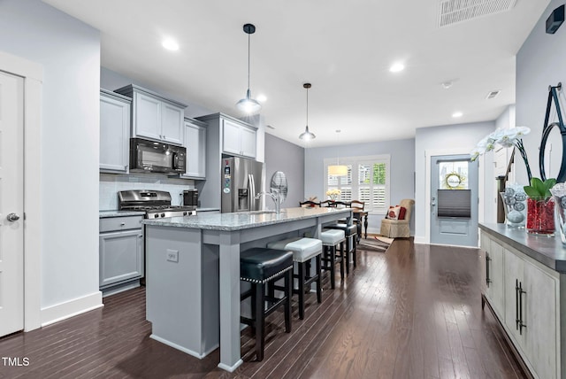 1448 Big Falls Dr, Wendell, NC 27591 - kitchen featuring stainless steel appliances, a center island with sink, gray cabinetry, a breakfast bar, and dark wood-type flooring