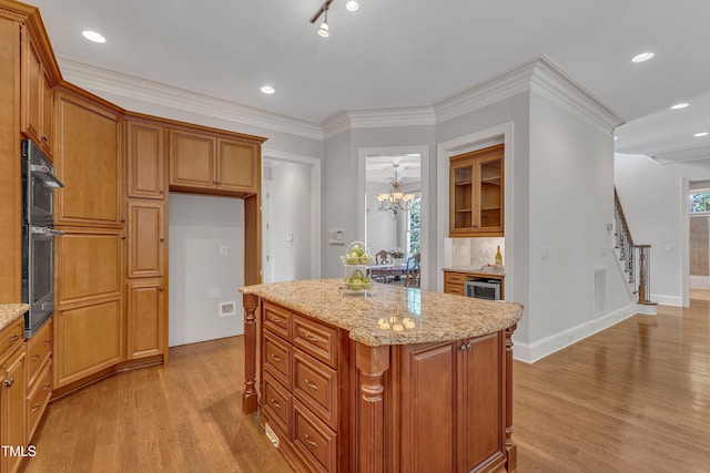 104 Bellagio Dr, Apex, NC 27539 - kitchen featuring light wood-style flooring, light stone counters, brown cabinets, a center island, and crown molding