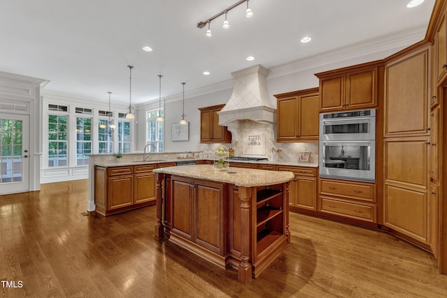 104 Bellagio Dr, Apex, NC 27539 - kitchen with a sink, a center island, custom exhaust hood, brown cabinetry, and a peninsula