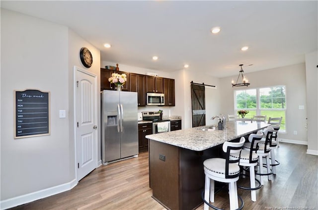 1865 John B Carter Rd, Fayetteville, NC 28312 - kitchen with stainless steel appliances, a barn door, a sink, dark brown cabinets, and light wood-type flooring