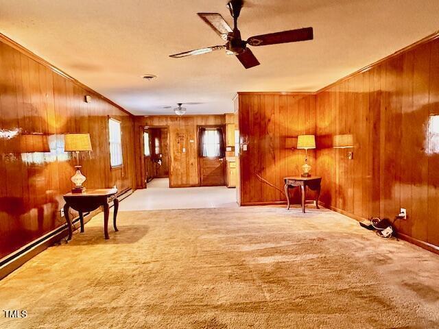 1007 Driftwood Dr, Siler City, NC 27344 - carpeted living room with wood walls, a ceiling fan, crown molding, and baseboard heating
