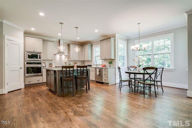 105 Everam Ct, Chapel Hill, NC 27516 - kitchen with stainless steel appliances, crown molding, wall chimney range hood, a breakfast bar, and backsplash