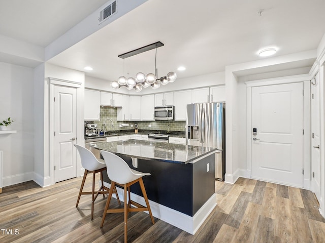 222 Glenwood Ave Unit 213, Raleigh, NC 27603 - kitchen featuring stainless steel appliances, tasteful backsplash, a center island, light wood-type flooring, and white cabinetry