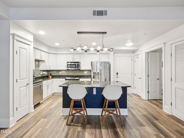 222 Glenwood Ave Unit 213, Raleigh, NC 27603 - kitchen with stainless steel appliances, a center island, light wood finished floors, tasteful backsplash, and white cabinets