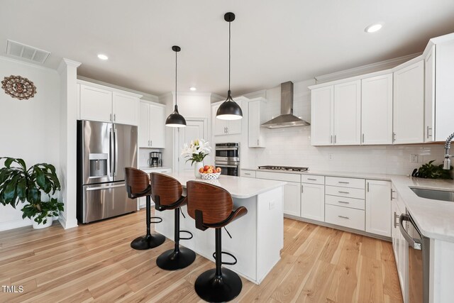 200 Cloud Berry Ln, Holly Springs, NC 27540 - kitchen featuring appliances with stainless steel finishes, wall chimney range hood, a kitchen island, light wood finished floors, and light countertops
