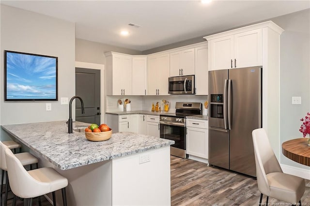 3029 Candlelight Dr, Fayetteville, NC 28311 - kitchen with stainless steel appliances, wood finished floors, white cabinetry, light stone countertops, and recessed lighting