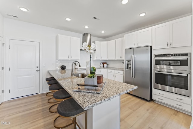 138 N White St # 100, Wake Forest, NC 27587 - kitchen featuring stainless steel appliances, wall chimney range hood, a breakfast bar area, white cabinetry, and light stone countertops