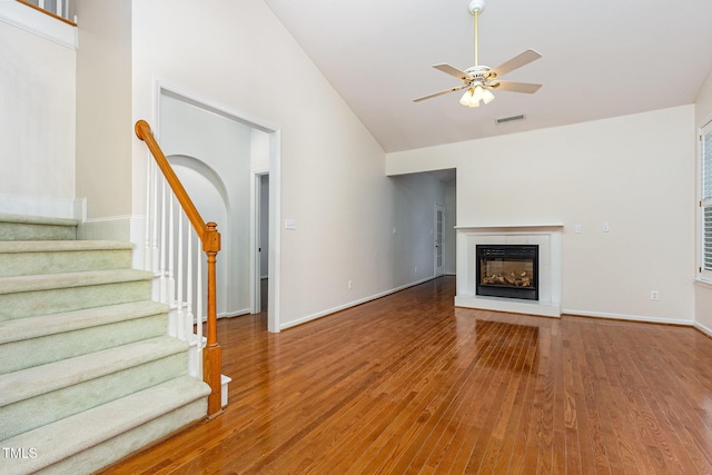 11005 Louson Pl, Raleigh, NC 27614 - unfurnished living room featuring ceiling fan, wood finished floors, high vaulted ceiling, stairs, and a glass covered fireplace