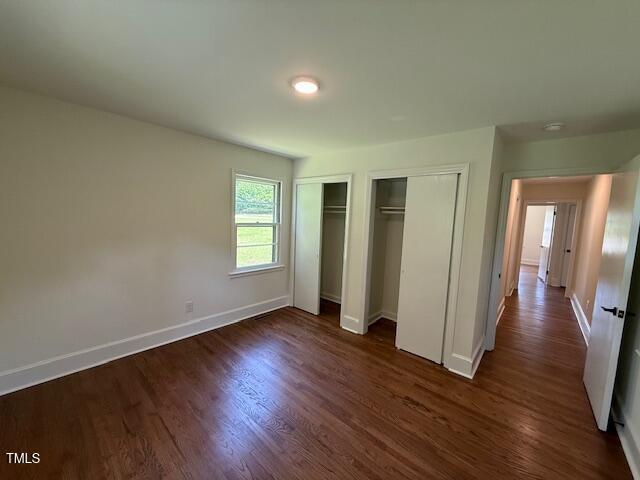 902 Roanoke Ave, Henderson, NC 27536 - unfurnished bedroom with multiple closets, baseboards, and dark wood-style flooring
