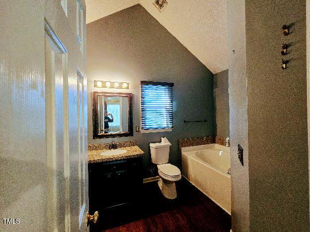 5301 Peacenest Dr, Raleigh, NC 27610 - full bathroom featuring a garden tub, lofted ceiling, vanity, toilet, and wood finished floors
