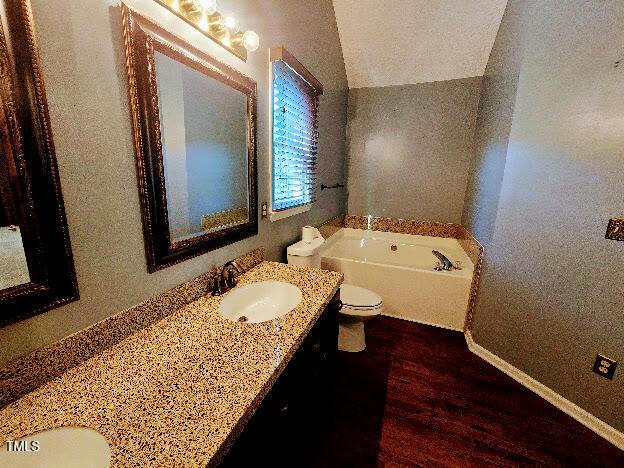 5301 Peacenest Dr, Raleigh, NC 27610 - full bath with double vanity, wood finished floors, toilet, a bath, and vaulted ceiling