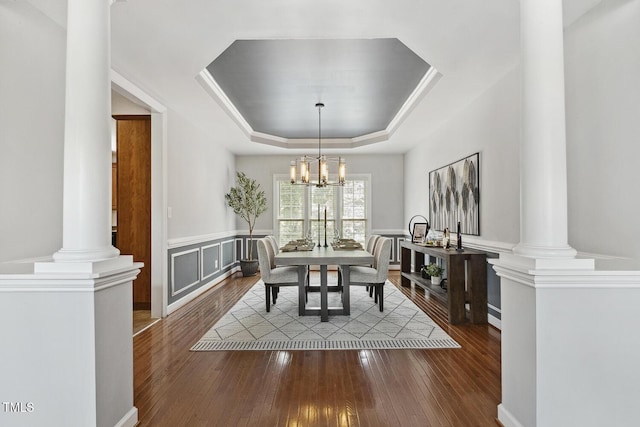 825 Highwater Pl, Fuquay Varina, NC 27526 - dining room with decorative columns, a tray ceiling, wood-type flooring, wainscoting, and a chandelier