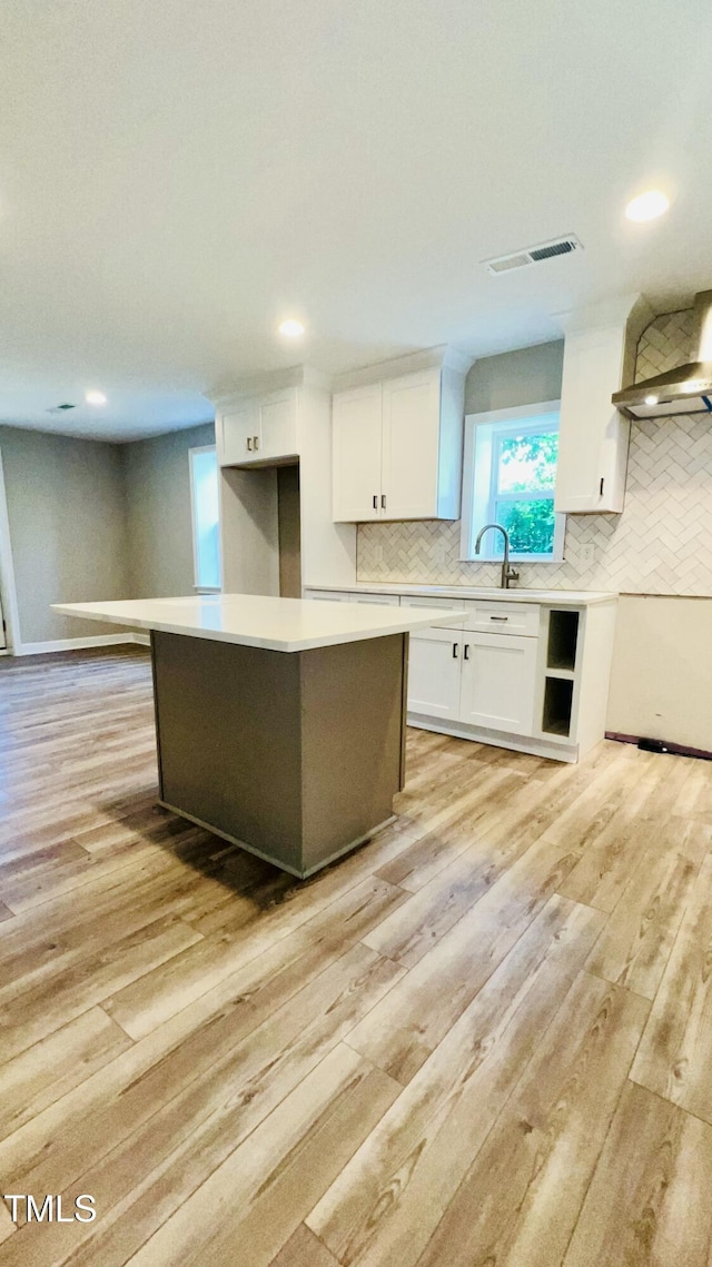 505 E Canary St, Dunn, NC 28334 - kitchen featuring wall chimney range hood, white cabinetry, light wood-type flooring, tasteful backsplash, and light countertops