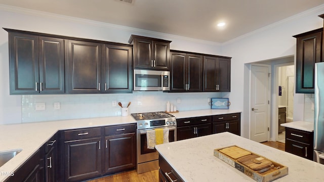 421 Old Ride Dr, Holly Springs, NC 27540 - kitchen featuring appliances with stainless steel finishes, backsplash, wood finished floors, light stone counters, and crown molding