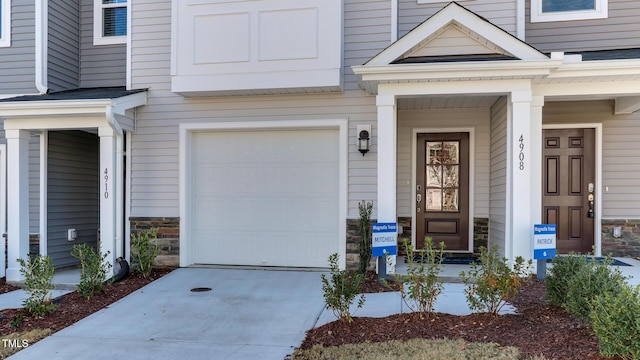 219 Carova Bnd, Apex, NC 27539 - property entrance featuring a garage, stone siding, and concrete driveway
