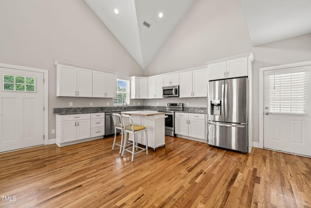 225 E End Ave, Durham, NC 27703 - kitchen with stainless steel appliances, white cabinets, a breakfast bar, light wood-style flooring, and high vaulted ceiling