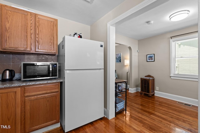 2710 Broad St, Durham, NC 27704 - kitchen featuring freestanding refrigerator, stainless steel microwave, arched walkways, tasteful backsplash, and wood finished floors