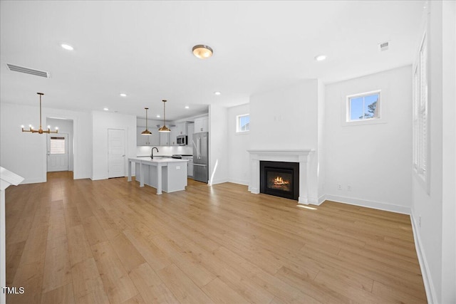 212 Aubey Ln, Wake Forest, NC 27587 - unfurnished living room with a glass covered fireplace, healthy amount of natural light, a chandelier, light wood-style flooring, and recessed lighting