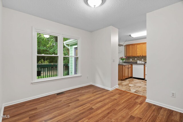 2724 Glastonbury Rd, Apex, NC 27539 - kitchen with white dishwasher, light wood-style floors, a textured ceiling, brown cabinets, and backsplash