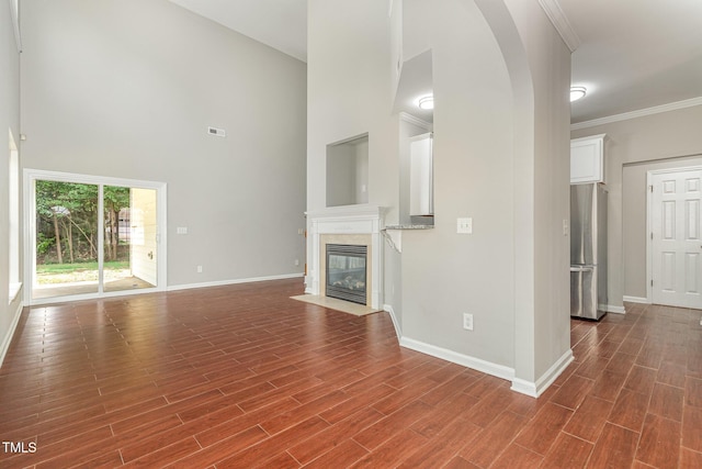 2409 Valley Haven Dr, Raleigh, NC 27603 - unfurnished living room with a high ceiling, a tiled fireplace, arched walkways, dark wood-type flooring, and crown molding