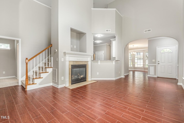 2409 Valley Haven Dr, Raleigh, NC 27603 - unfurnished living room featuring a high ceiling, arched walkways, a tiled fireplace, wood finished floors, and stairs