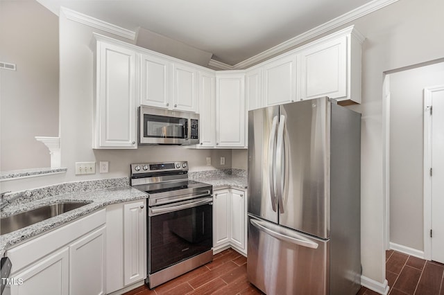 2409 Valley Haven Dr, Raleigh, NC 27603 - kitchen with stainless steel appliances, wood finish floors, white cabinetry, light stone counters, and ornamental molding