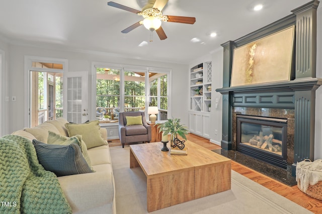 314 Chanticlair Dr, Apex, NC 27502 - living room featuring light wood-type flooring, a premium fireplace, ceiling fan, crown molding, and built in shelves