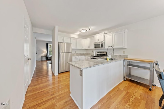 72 Justin Ct, Durham, NC 27705 - kitchen featuring appliances with stainless steel finishes, a sink, a peninsula, white cabinets, and light wood-type flooring