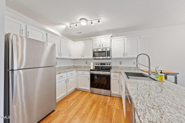 72 Justin Ct, Durham, NC 27705 - kitchen with appliances with stainless steel finishes, a sink, white cabinetry, light wood finished floors, and light stone countertops