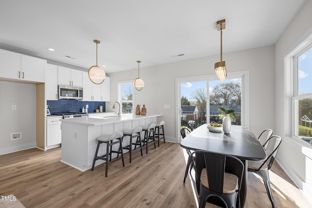 517 Coleman St, Raleigh, NC 27610 - kitchen with stainless steel microwave, a breakfast bar, light wood-style floors, decorative backsplash, and white cabinets