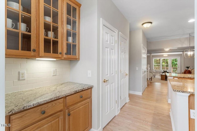 4724 Ludwell Branch Ct, Raleigh, NC 27612 - kitchen featuring light wood-style floors, decorative backsplash, light stone countertops, glass insert cabinets, and baseboards