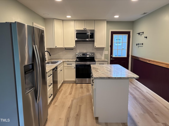 301 Roseland Ave, Durham, NC 27712 - kitchen featuring appliances with stainless steel finishes, a kitchen island, light stone countertops, light wood-type flooring, and white cabinetry