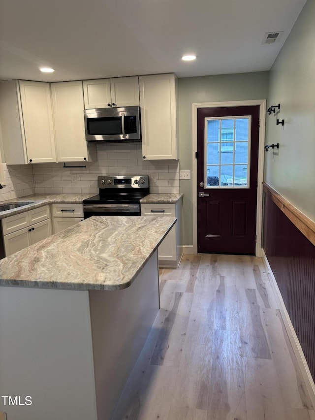 301 Roseland Ave, Durham, NC 27712 - kitchen featuring stainless steel appliances, white cabinetry, light wood-style flooring, tasteful backsplash, and light stone counters