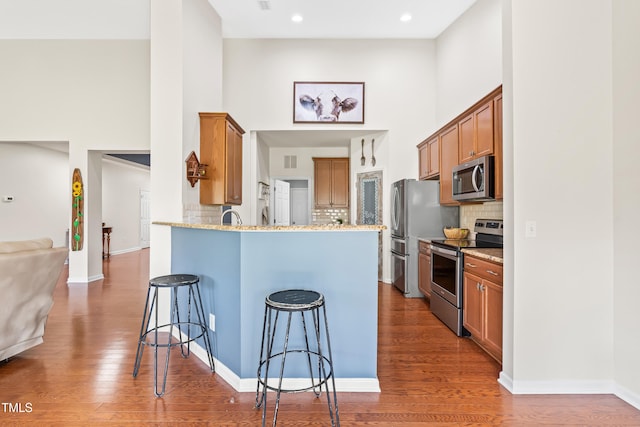 1400 Manley Ct, Fuquay Varina, NC 27526 - kitchen with stainless steel appliances, a towering ceiling, a breakfast bar area, a peninsula, and light stone counters