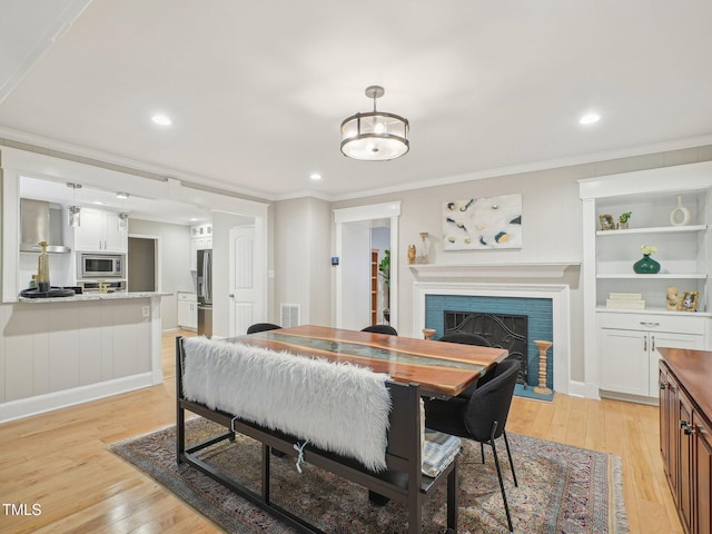 3934 Hope Valley Rd, Durham, NC 27707 - dining space featuring a brick fireplace, light wood-style floors, crown molding, built in shelves, and recessed lighting