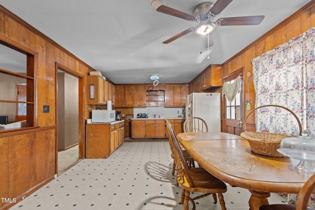 4038 Redwood Rd, Durham, NC 27704 - kitchen with white appliances, ornamental molding, wood walls, brown cabinets, and ceiling fan