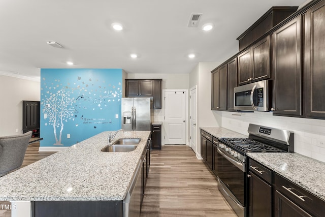 409 Rhamkatte Rd, Holly Springs, NC 27540 - kitchen with stainless steel appliances, a sink, dark brown cabinets, a kitchen island with sink, and light stone countertops